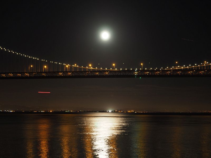 The moon reflects on the water below the Bay Bridge